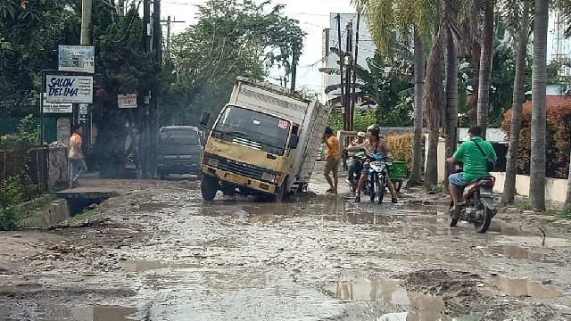 Mobil yang terperosok karena jalanan di Jalan Menteng II, Kelurahan Binjai, Kecamatan Medan Denai, yang berlumpur dan berlubang, yang rusak akibat pembuatan drainase bawah tanah yang ditinggal begitu saja oleh Dinas PU Pemko Medan begitu proyek drainase selesai dikerjakan. (Jhonson Siahaan)